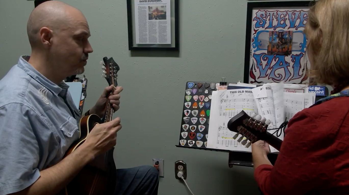 David Dunavant is teaching an adult student guitar techniques in a lesson.