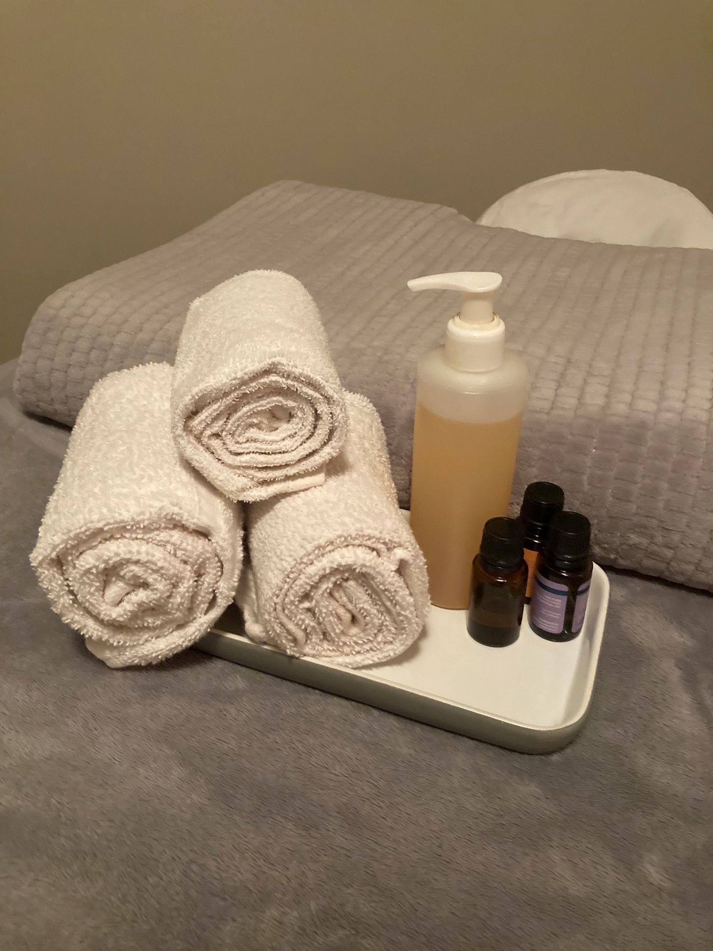 Massage oil, essential oils and rolled up towels in front of textured blanket