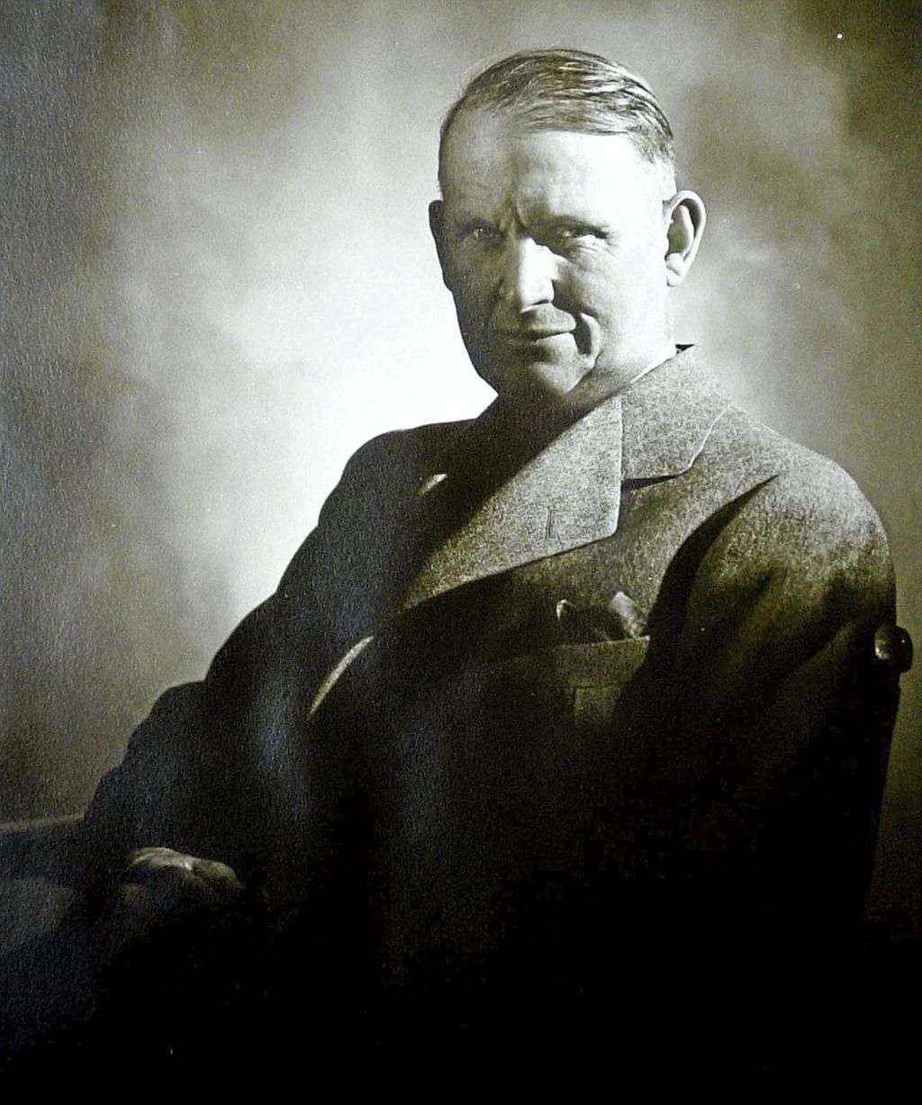 Man in a suit, seated. Dark, sepia-toned studio portrait. Looking towards the camera with a slight smile.