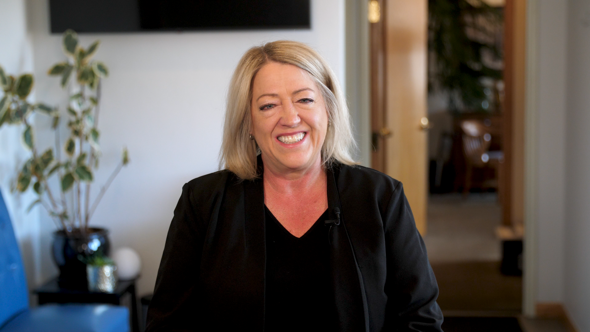 A woman in a black jacket is smiling in a waiting room.