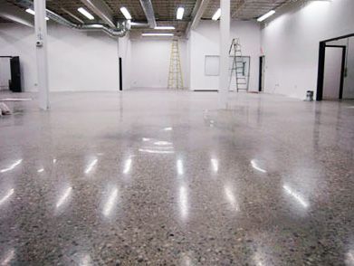 A large empty room with a ladder on the ceiling and a shiny concrete floor.