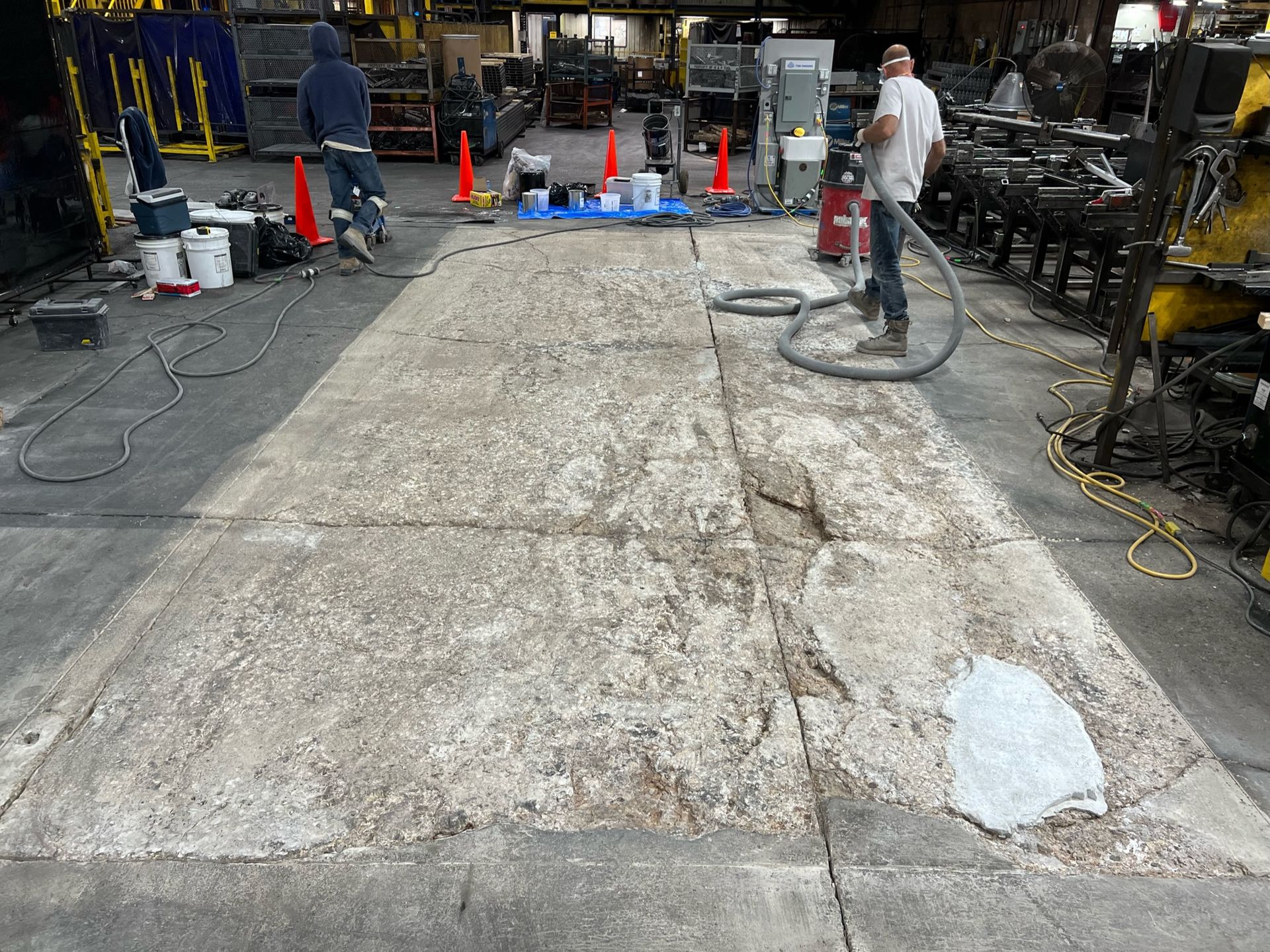 A man is using a vacuum cleaner to clean a concrete floor in a factory.