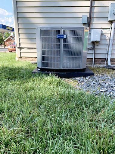 An air conditioner is sitting on the side of a house in the grass.