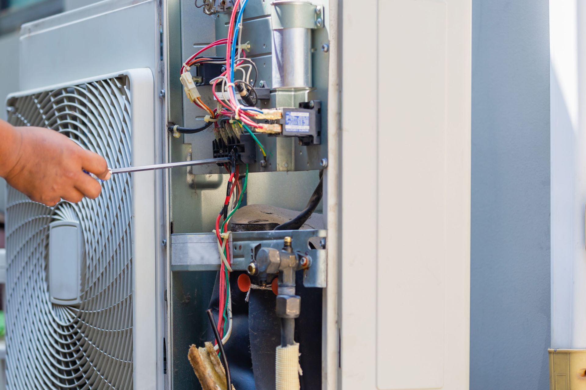 A man is fixing an air conditioner with a screwdriver.