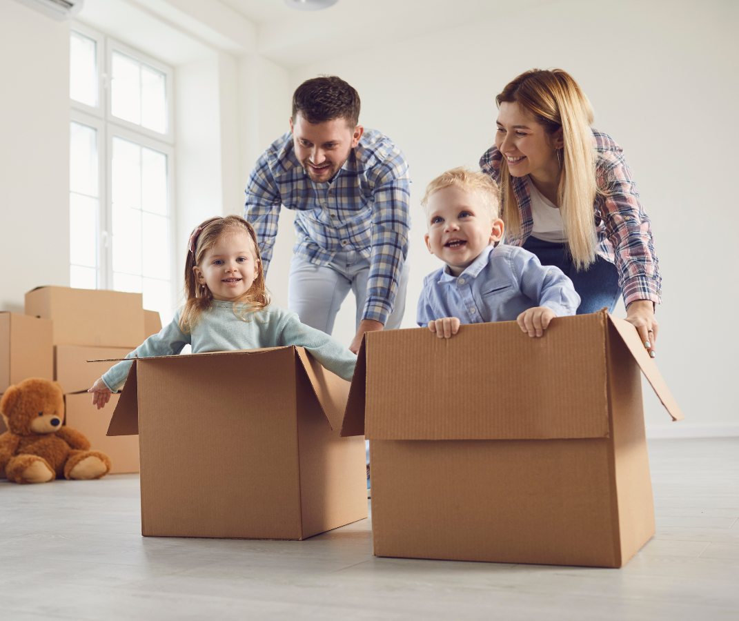 Family with two children in cardboard boxes in a bright moving room, smiling and playing