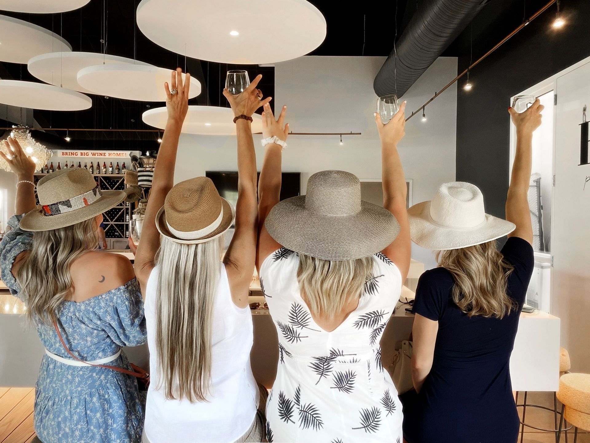 Four women wearing hats are standing next to each other with their arms in the air.