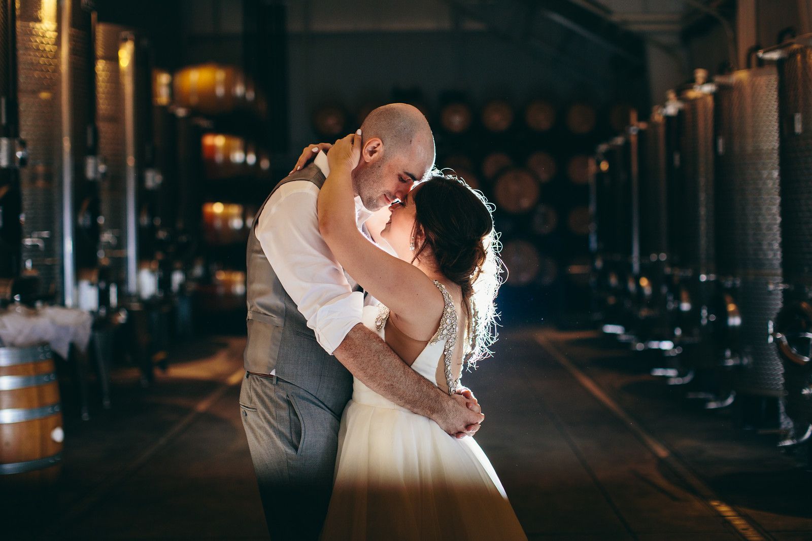 A bride and groom are kissing in a wine cellar.