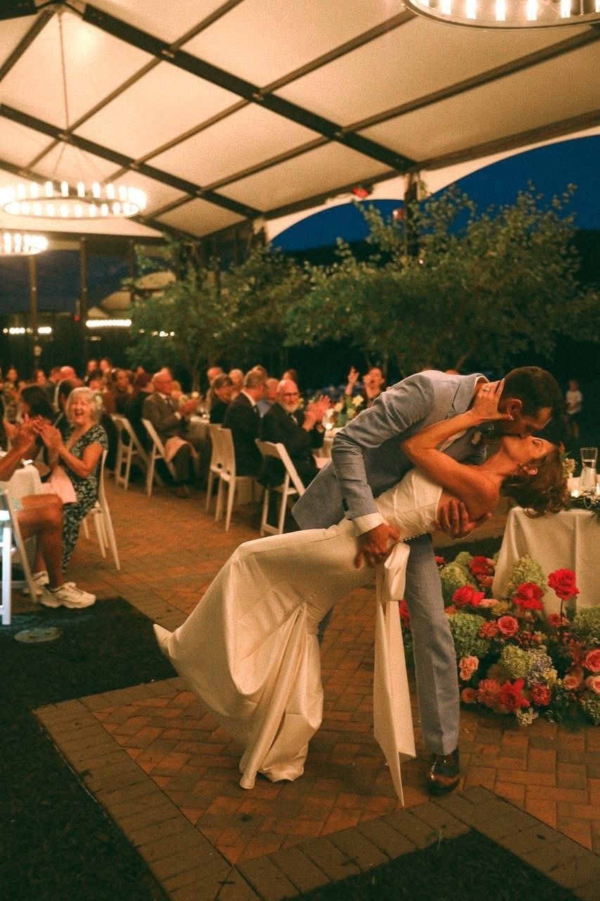 Couple kissing during a wedding reception dance.  Bride in white dress leans back as groom dips her on a dance floor.