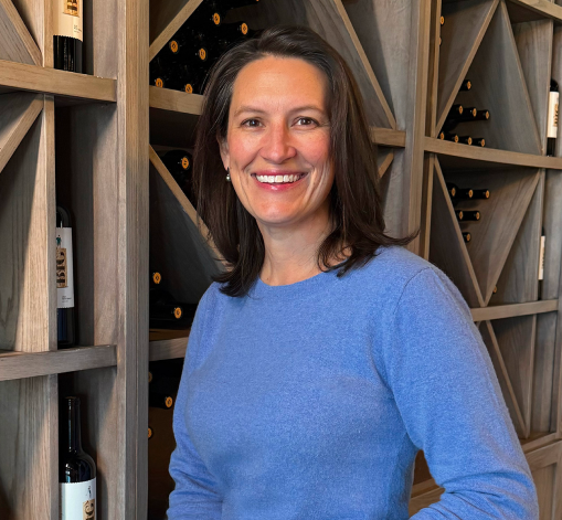 A woman in a blue sweater is holding a bottle of wine.