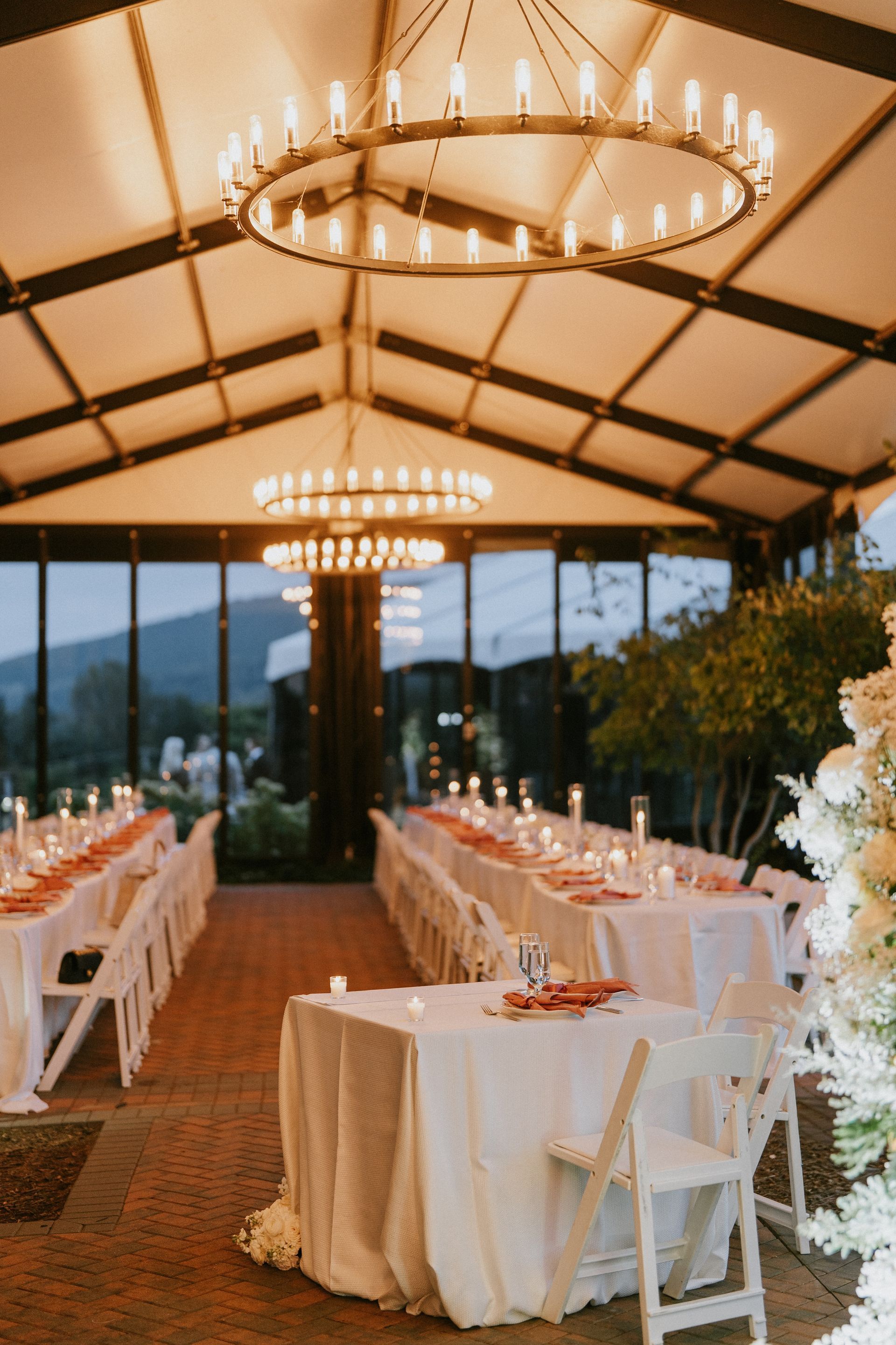 Elegant wedding reception hall with tables set for guests, under a warm-lit chandelier.