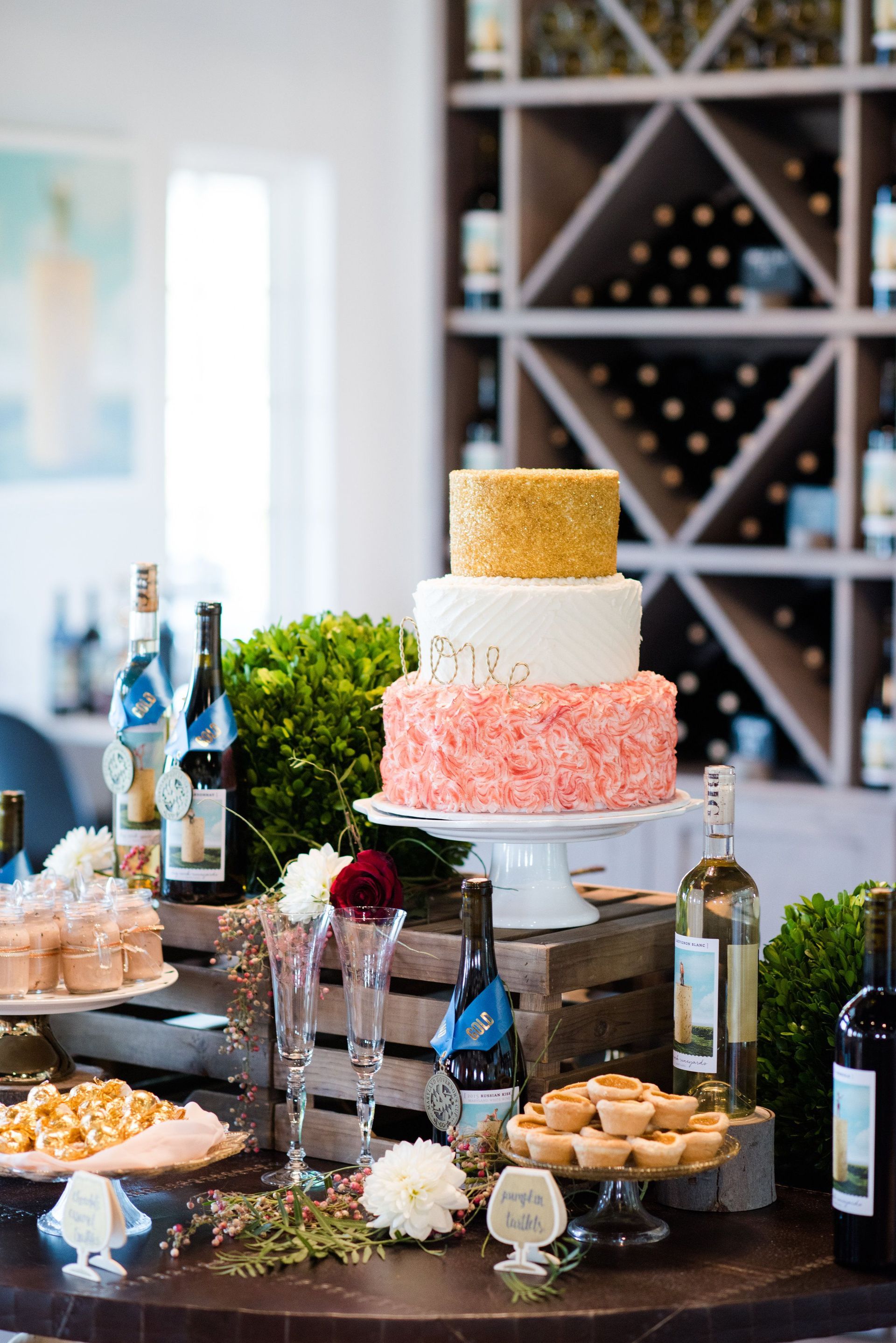 A table with a cake , cupcakes , and wine bottles on it.