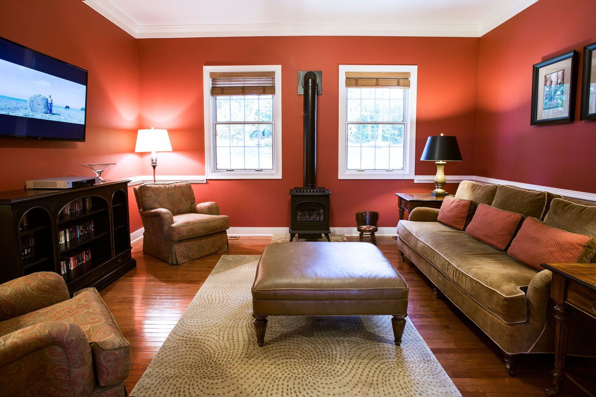 A living room with red walls , a couch , chairs , and a television.