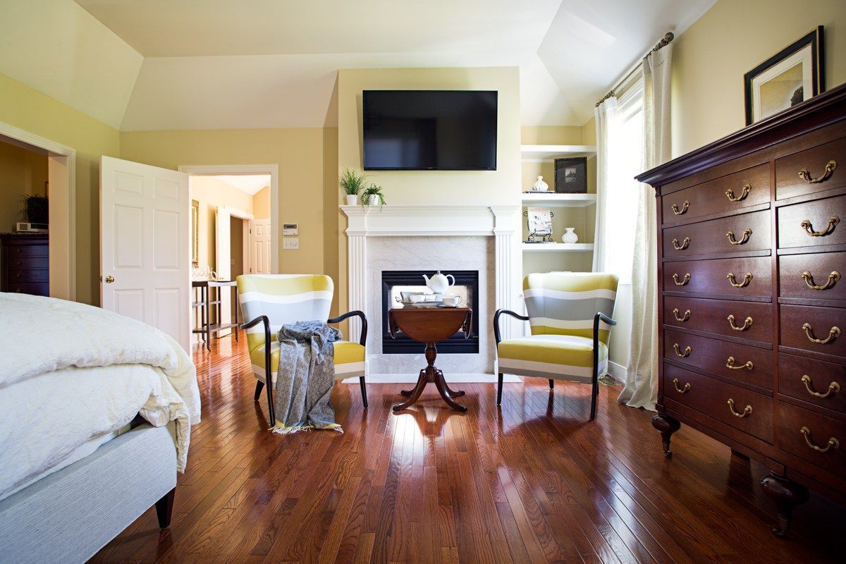A living room with a fireplace , chairs , a dresser and a flat screen tv.