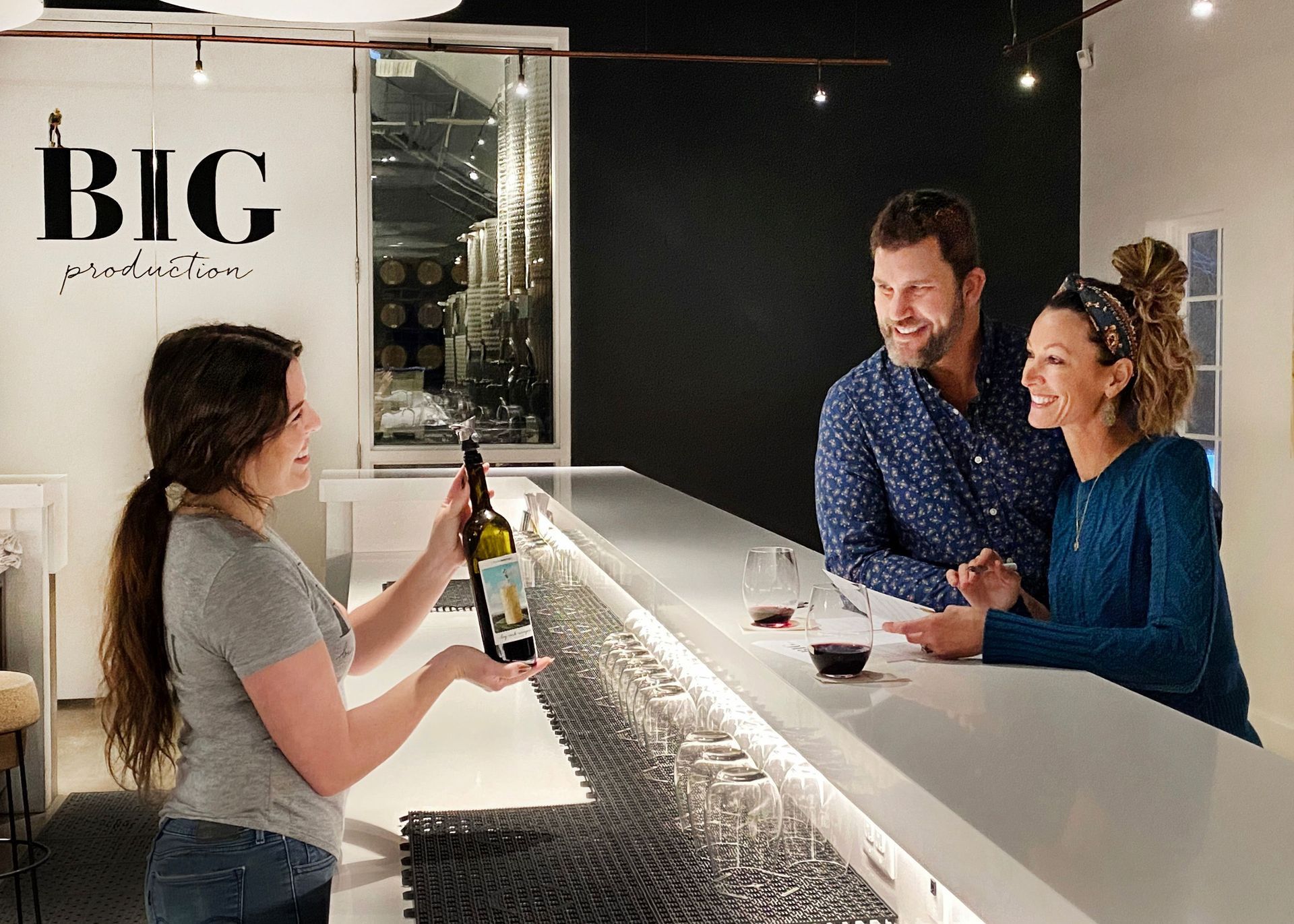A woman is serving a bottle of wine to a man and woman at a bar.