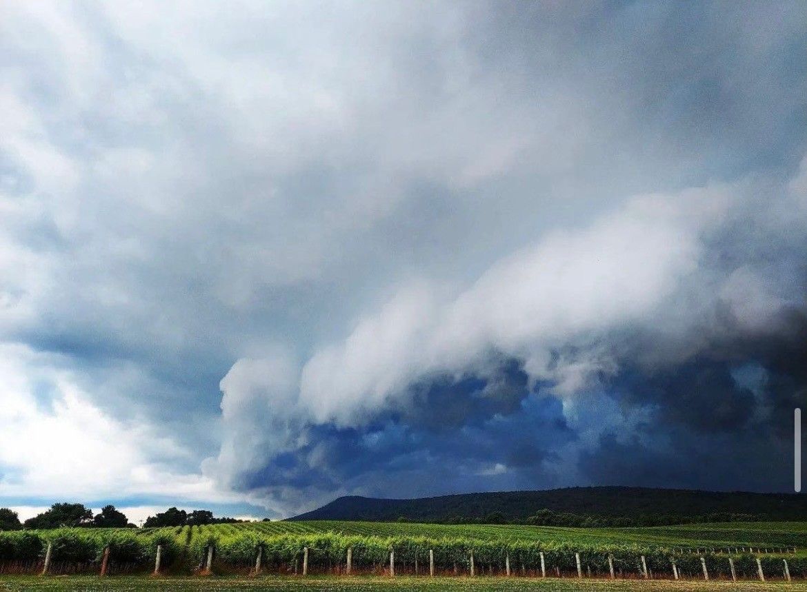 A cloudy sky over a field with a fence in the foreground