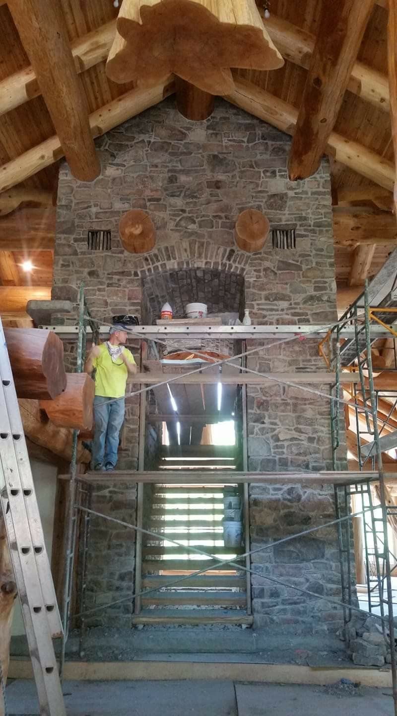 Stone fireplace under a timber roof, with scaffolding and a worker in a yellow shirt