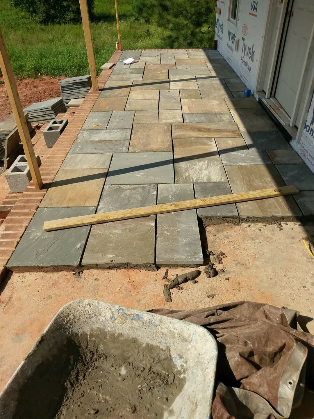 Stone pavers being installed on a walkway beside a building, with tools and construction materials nearby