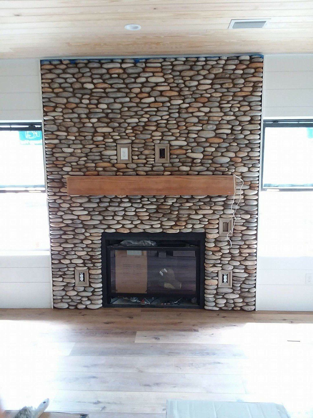 Stone fireplace with a wooden mantel in a bright, empty room with hardwood floors