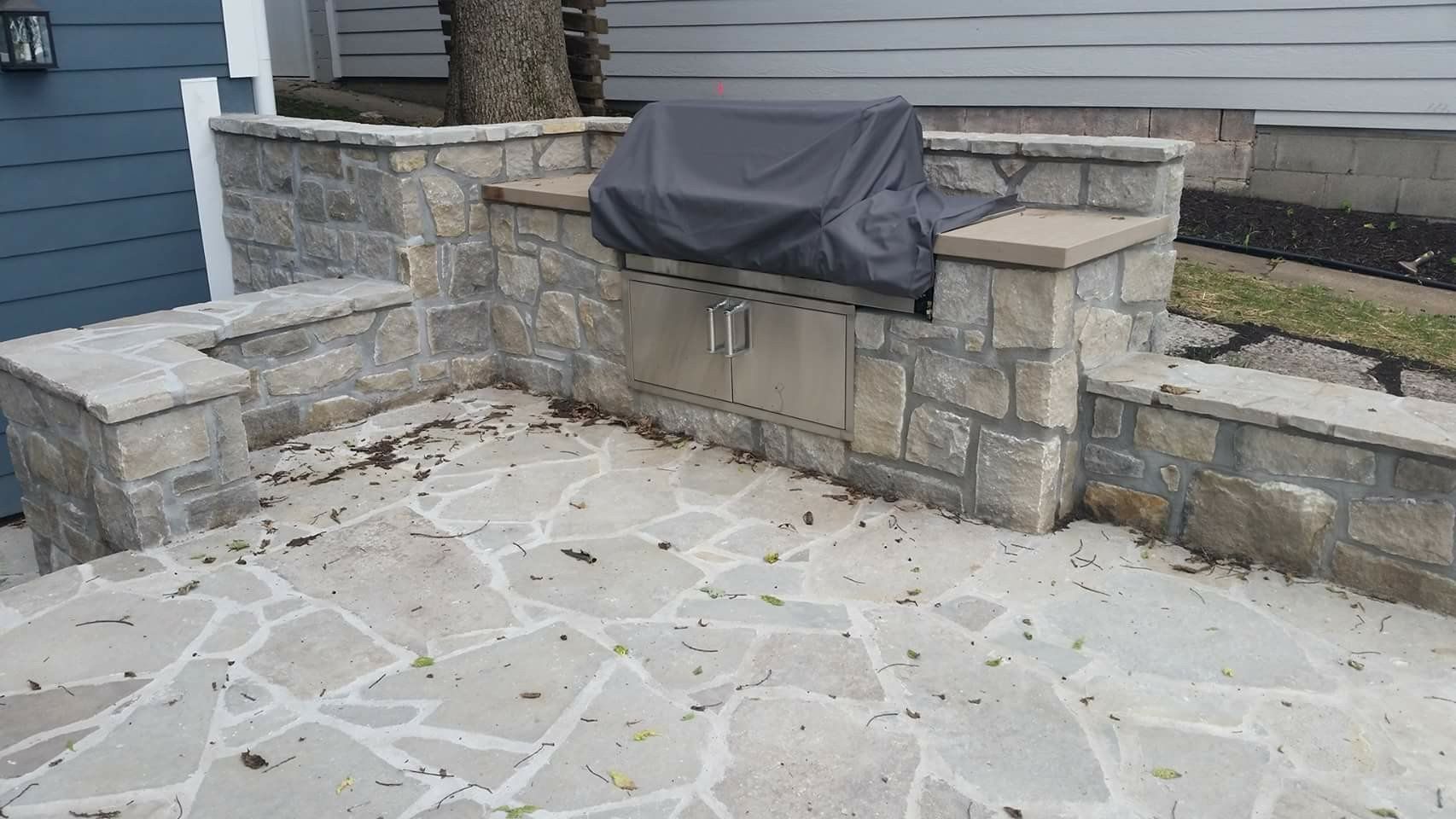Stone patio with built-in seating and a covered grill against a house exterior