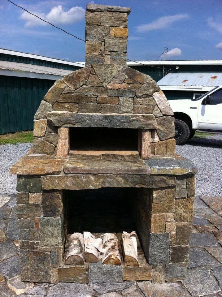 Stone outdoor fireplace or pizza oven with chimney and wood logs inside, in a yard.