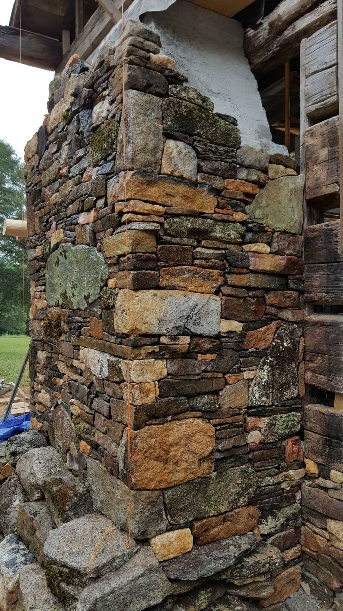Rustic stone wall corner with stacked rocks and a round green plaque outdoors