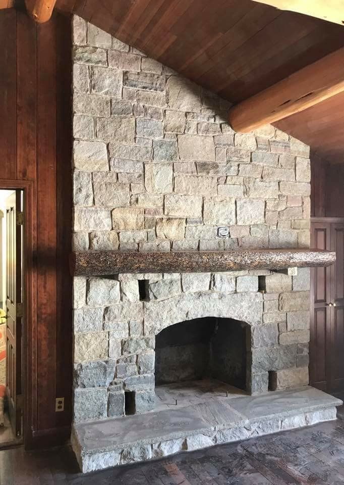 Stone fireplace with mantel in a wood-paneled room beneath a sloped ceiling