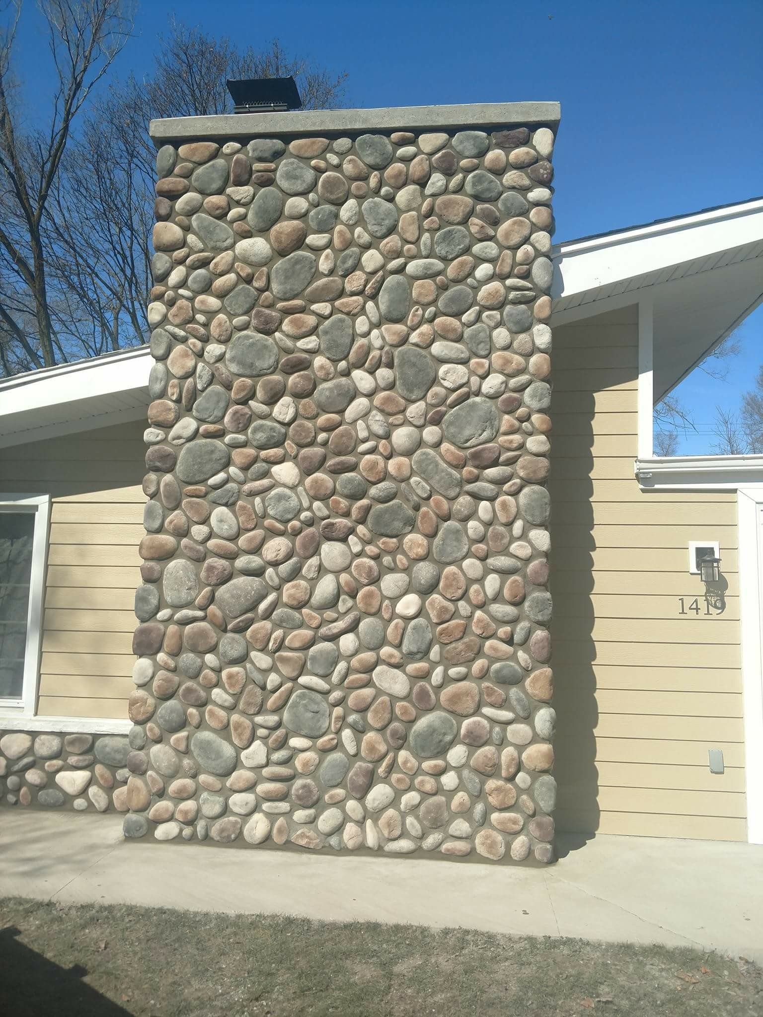 Stone chimney on a beige house under a clear blue sky.