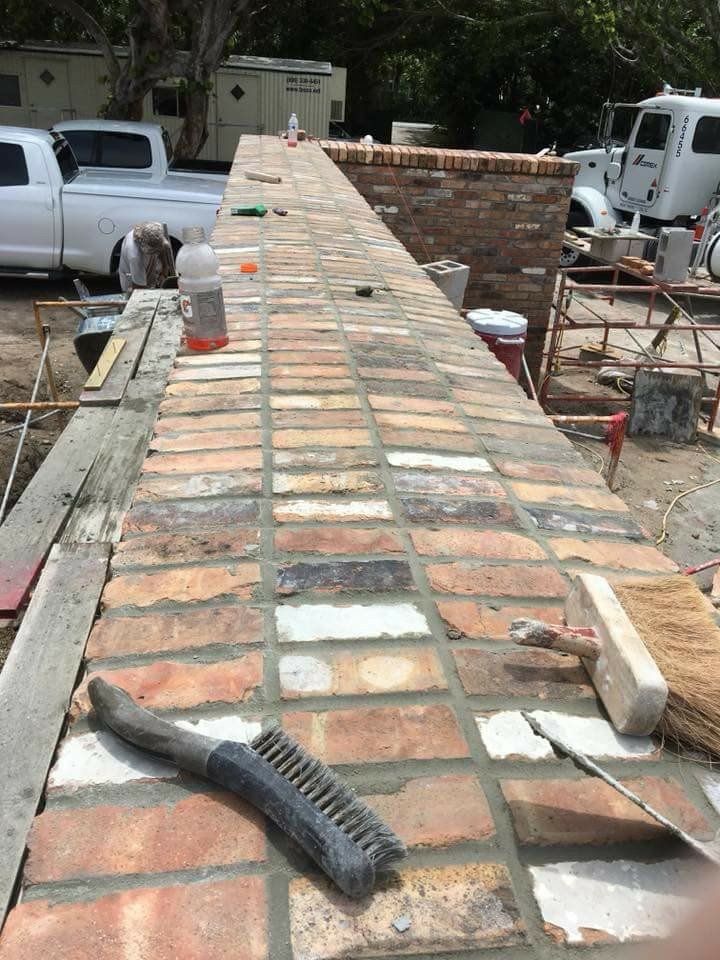 Brick wall under construction with workers' tools on top, seen from a rooftop.