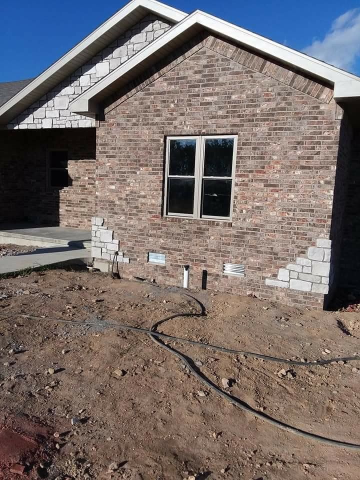 Brick house exterior under construction with unfinished dirt yard and window centered on the wall