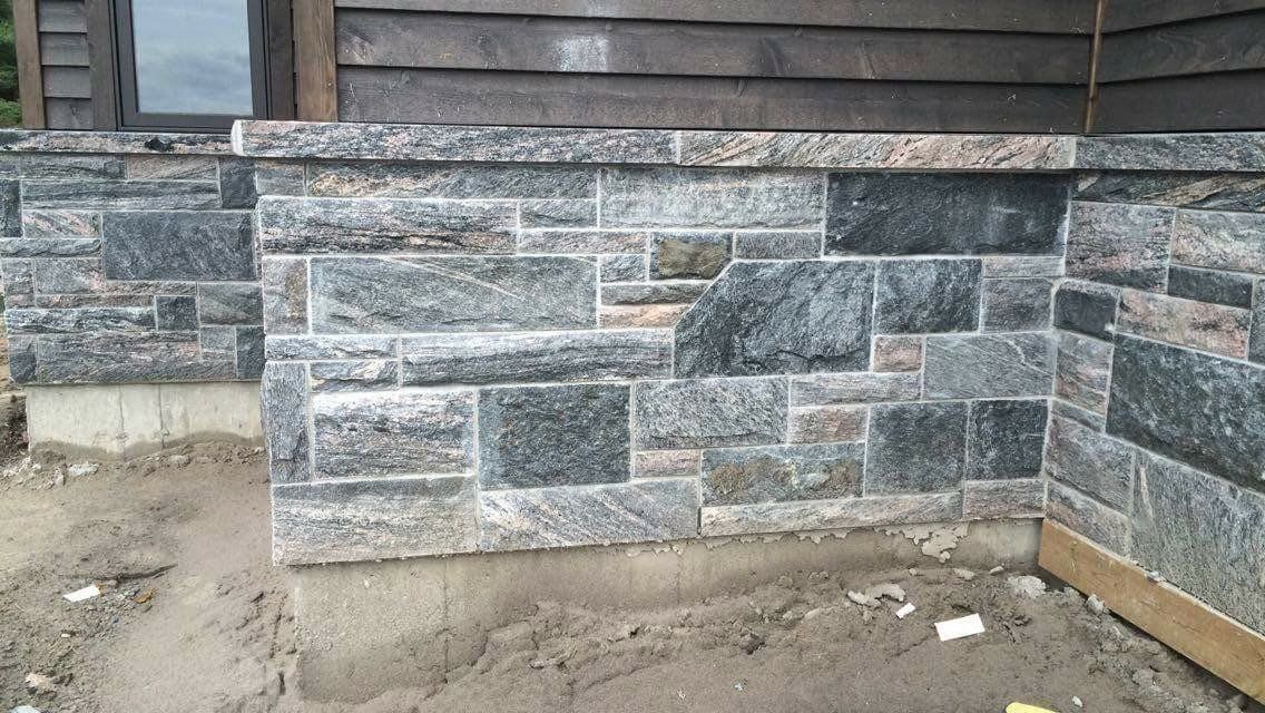Stone foundation wall beneath wooden siding with unfinished dirt along the base