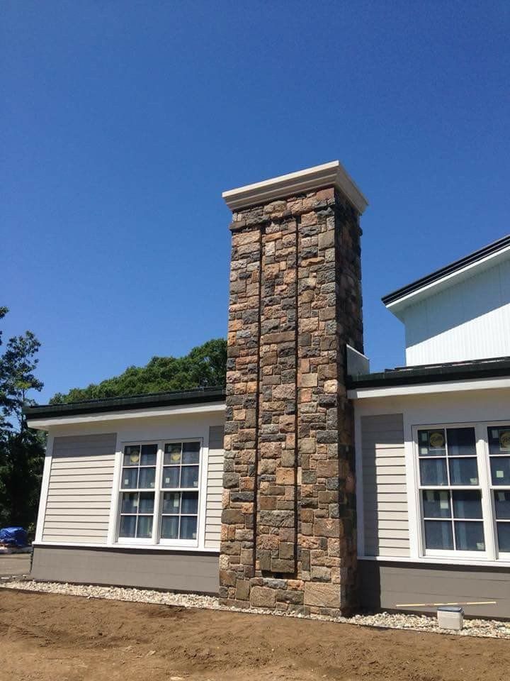 Exterior of a building with a tall stone chimney, beige siding, white-trimmed windows, and a blue sky