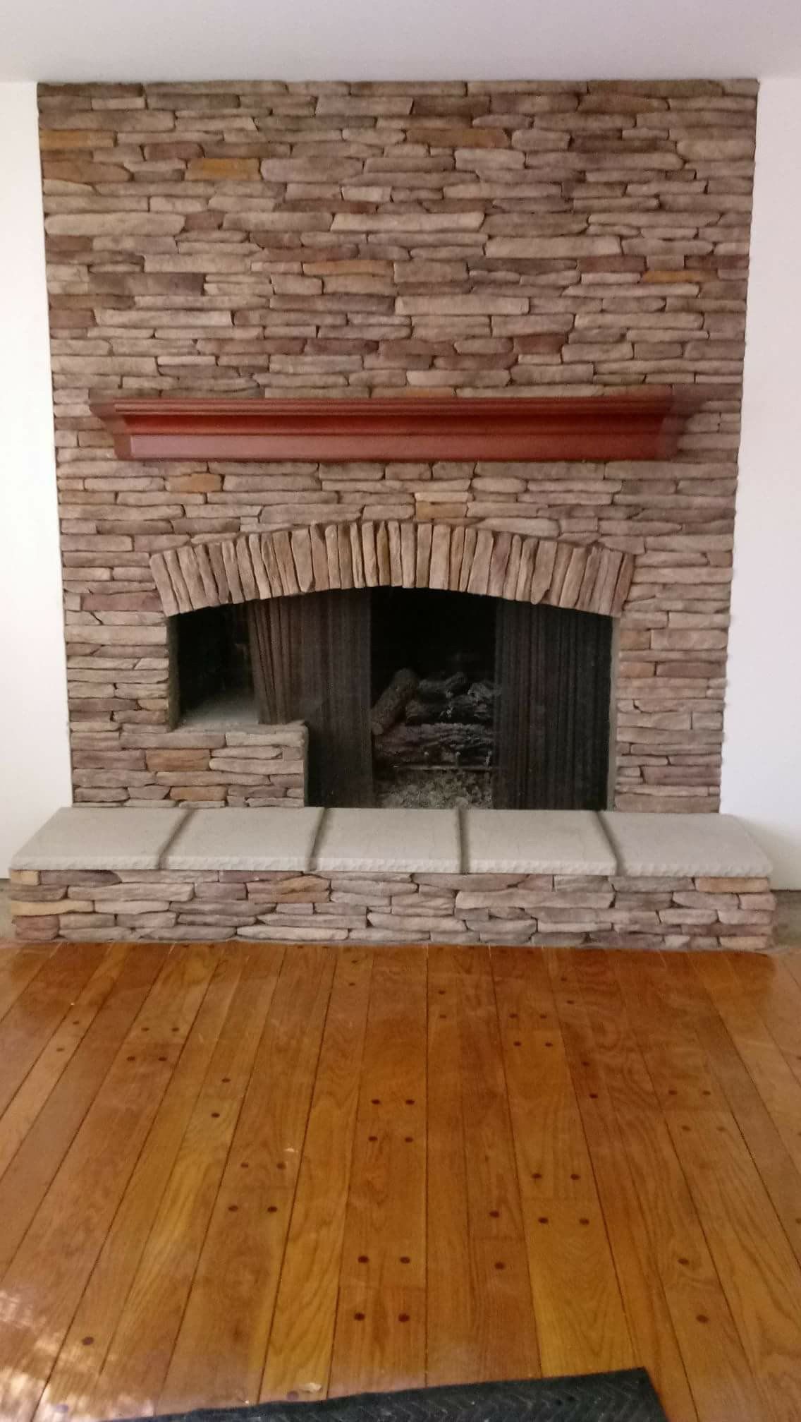 Stone fireplace with arched black opening, red mantel, and wooden floor in a room