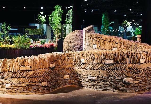 Nighttime garden sculpture of stacked wood and stone with a curved wall and lit plants