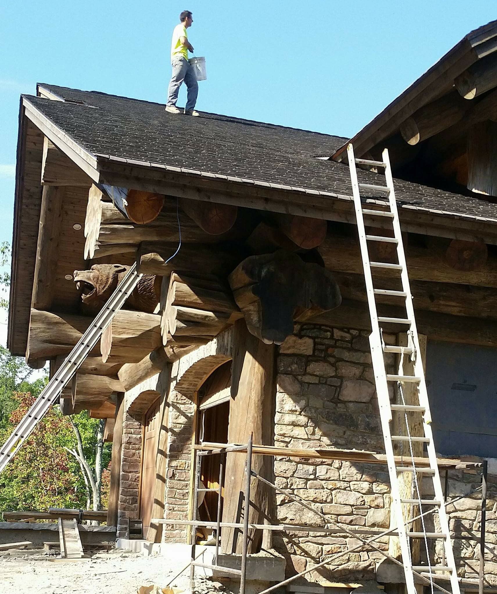Two workers repair a stone and wood roof, with one standing on top and a ladder leaning against the wall.