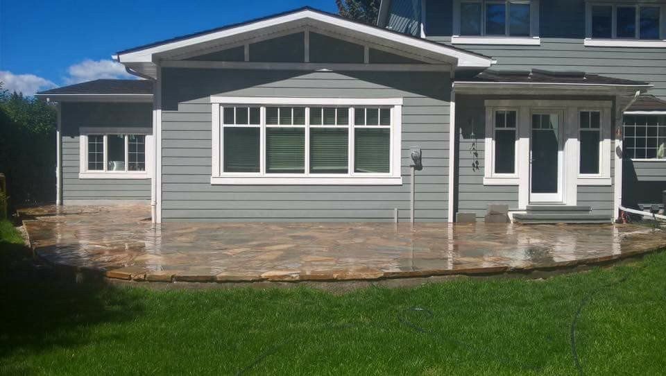 Gray house with white trim, large front windows, and a stone patio in a sunny yard