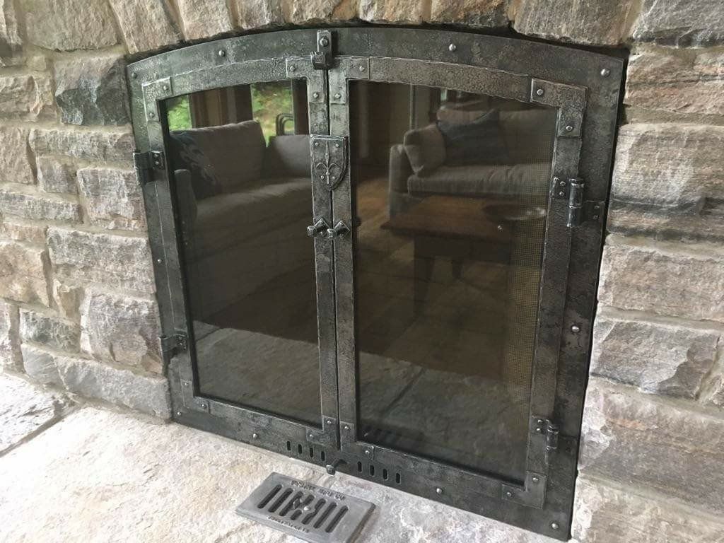 Dark metal fireplace door with tinted glass set in a stone wall above a floor vent