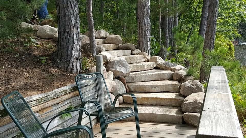 Stone steps leading up a wooded hillside beside a bench and railing on a deck
