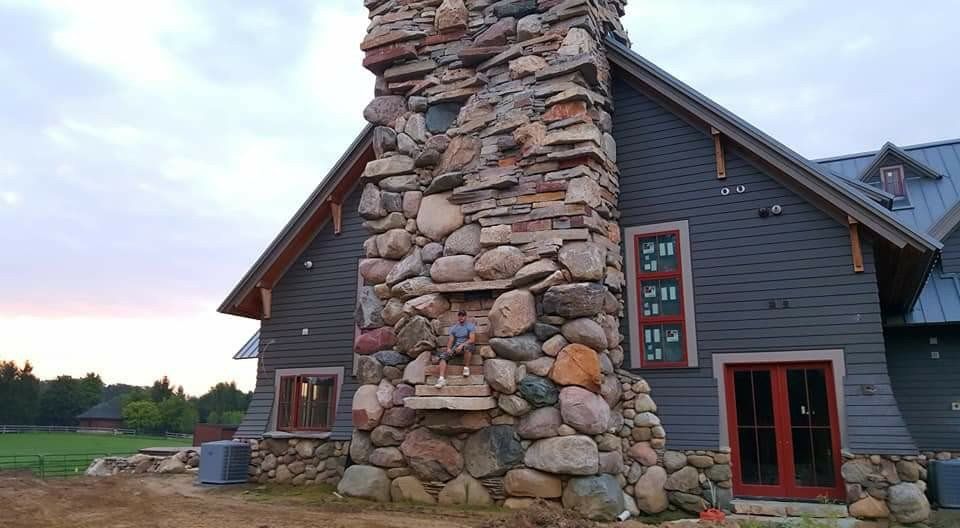 Stone chimney on a dark gray house at dusk, with red-trimmed doors and windows.