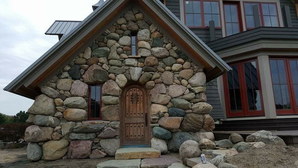 Small stone cottage facade with arched wooden door and red-trimmed windows