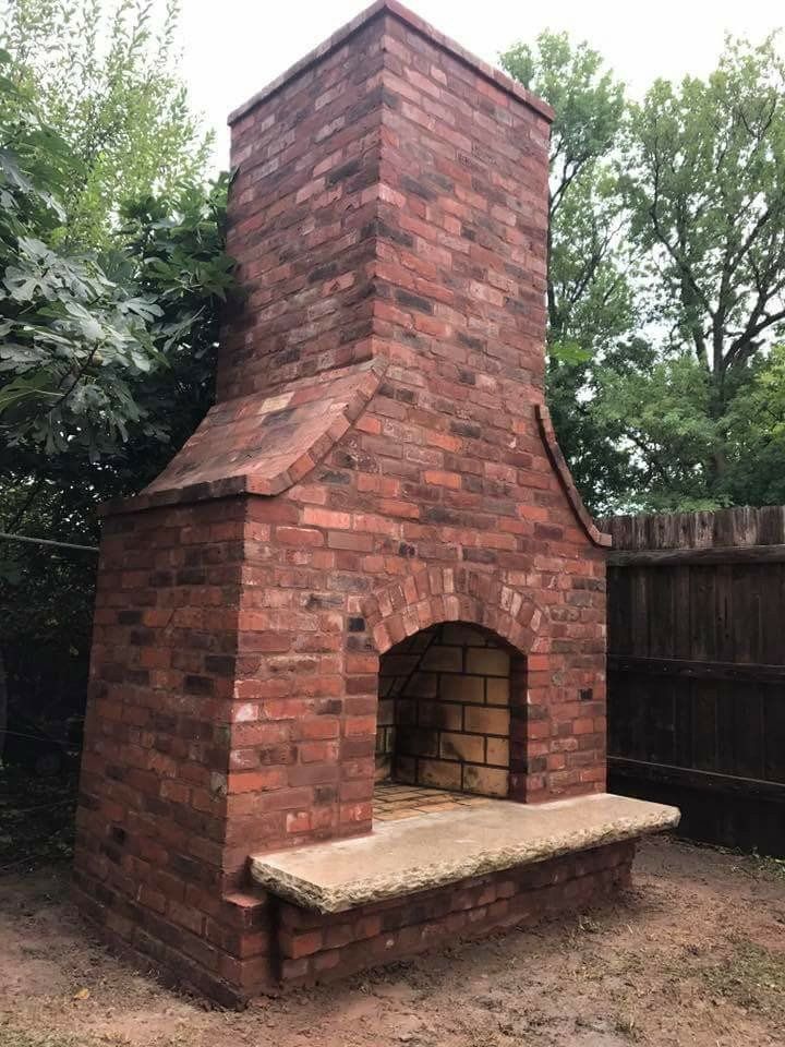 Brick outdoor fireplace with tall chimney and arched firebox opening in a backyard