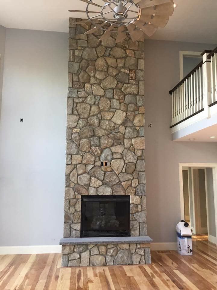 Living room with a tall stone fireplace, light wood floors, and an upstairs balcony railing