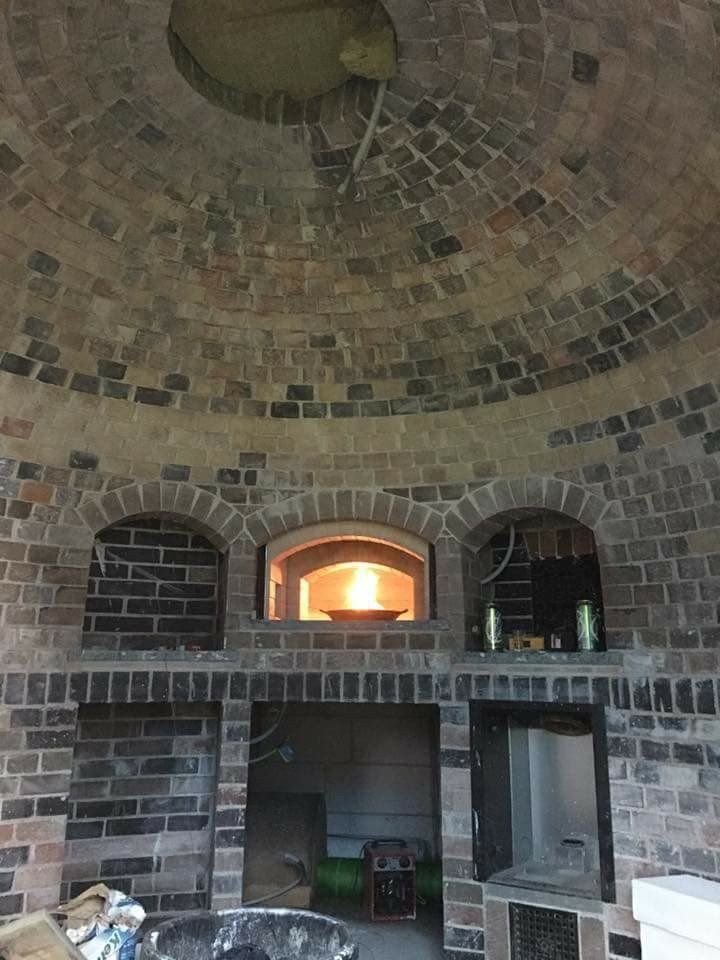 Stone brick outdoor oven with arched openings and a glowing fire inside, under a domed brick ceiling