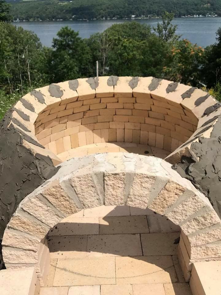 Stone outdoor fire pit overlooking a lake, with brick-lined interior and arched stone openings