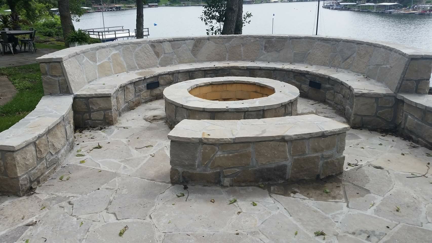 Stone circular fire pit with curved benches on a paved patio by the water