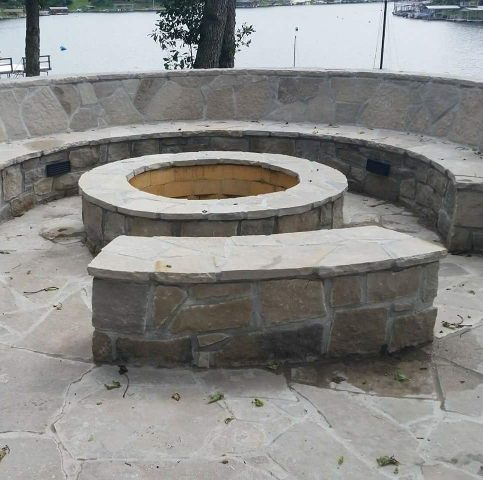 Stone fire pit with circular bench seating in an outdoor paved area near water