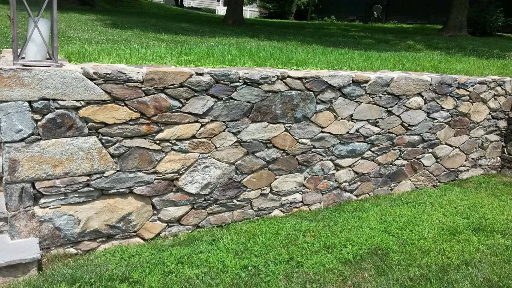 Stone retaining wall beside a green lawn, built with mixed gray and tan rocks.