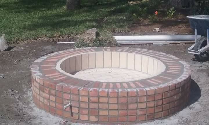 Round brick fire pit with light tan interior in a backyard setting.