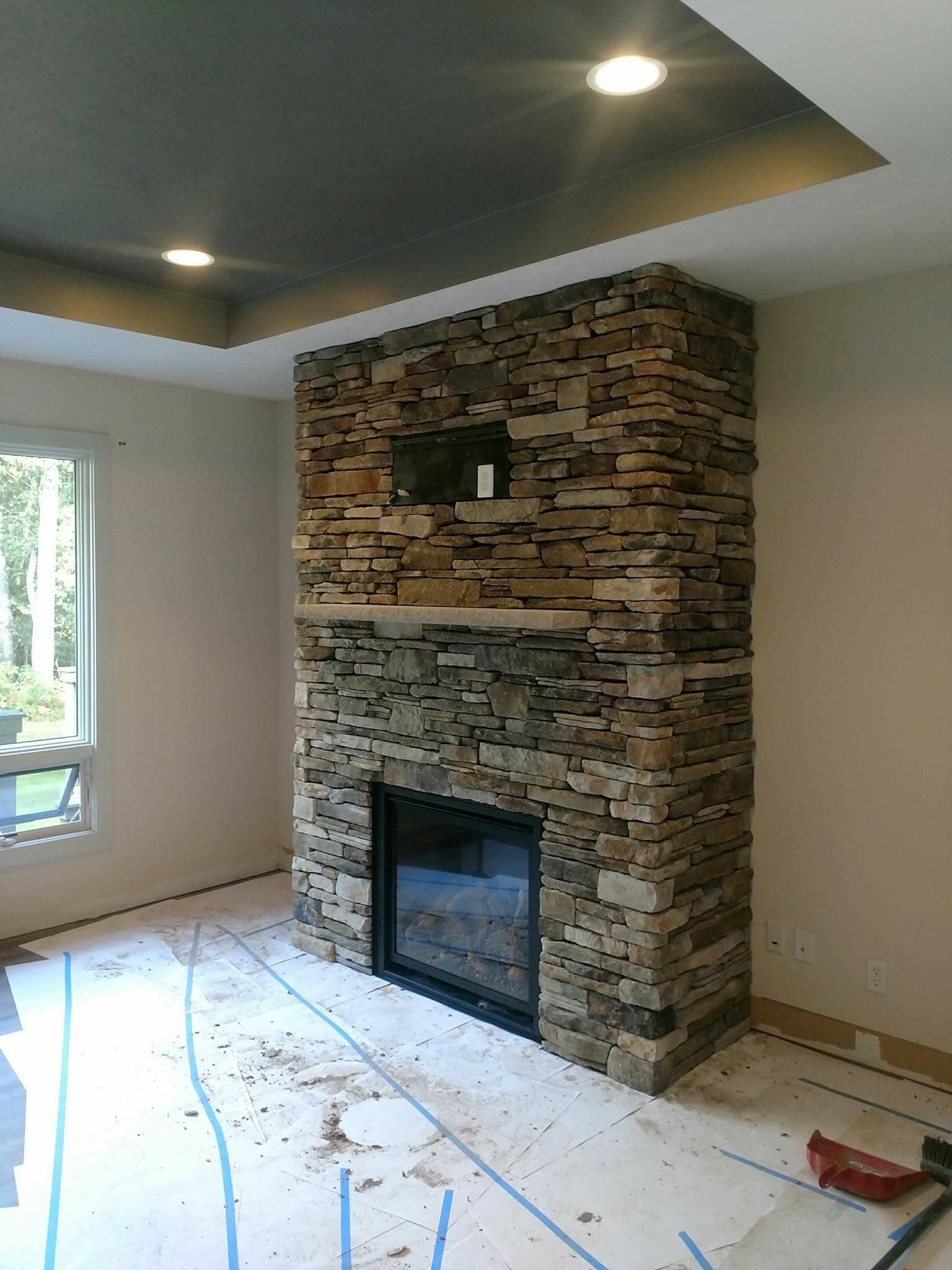 Living room with a stacked-stone fireplace under construction and tools on the floor.