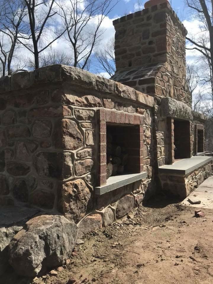 Stone outdoor fireplace with a tall chimney and built-in benches under a blue sky