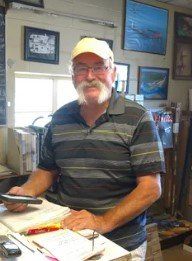Man in a striped shirt and cap standing behind a counter in a framed-art shop